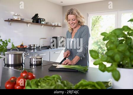 Smiling woman cutting spring onions in kitchen Stock Photo