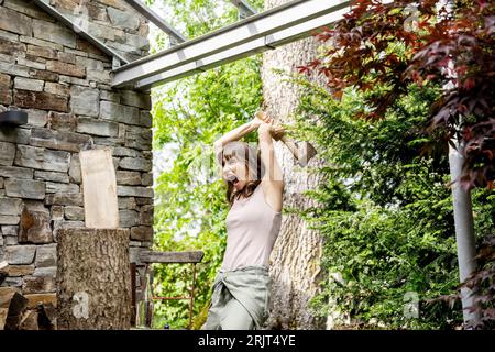 Screaming woman chopping wood in front of a house Stock Photo
