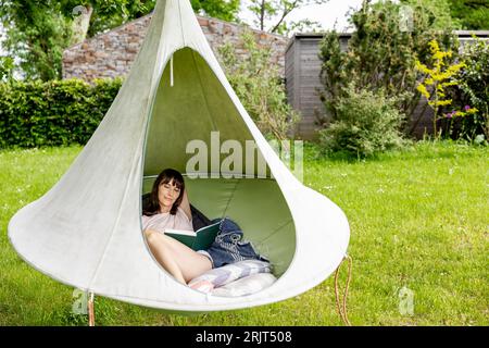 Relaxed woman reading book in a hanging tent Stock Photo