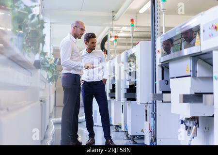 Male technicians checking remote control of machinery at factory Stock Photo