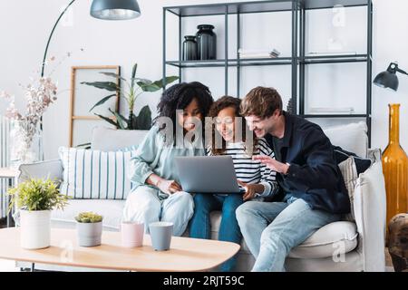 Laughing parents sitting on sofa with daughter watching laptop Stock Photo
