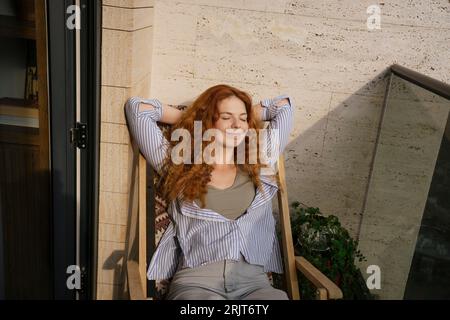 Smiling woman resting on chair in balcony Stock Photo