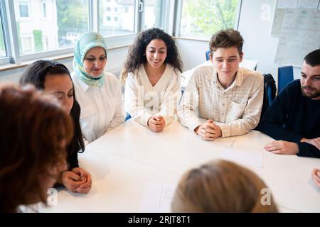 Students sitting with hands clasped around table in classroom Stock Photo