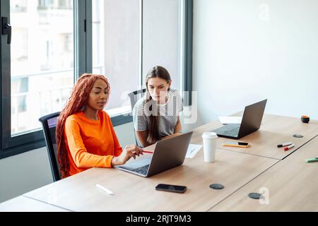 Smiling businesswoman having discussion with colleague over laptop Stock Photo