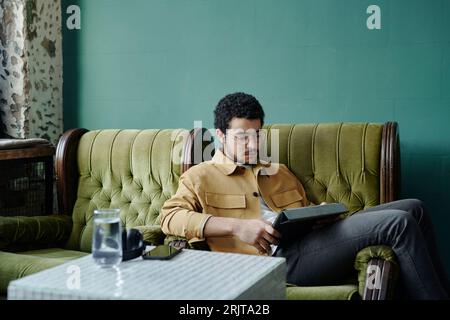 Young businessman sitting relaxed in green armchair and using tablet PC Stock Photo