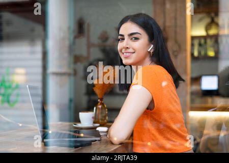 Smiling young businesswoman with laptop sitting in cafe Stock Photo