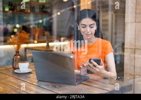 Smiling freelancer using smart phone in cafe Stock Photo
