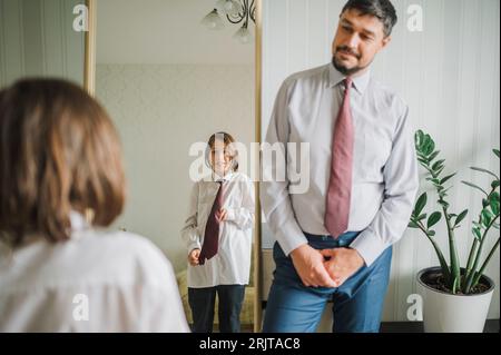 Father looking at son trying necktie in front of mirror at home Stock Photo