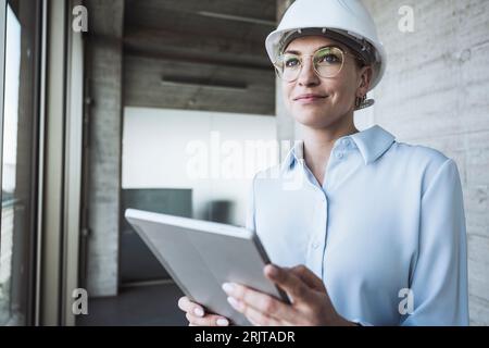 Smiling engineer wearing hardhat standing with tablet PC Stock Photo