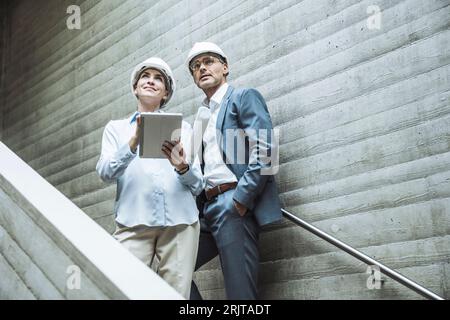 Thoughtful architects standing with tablet PC on staircase Stock Photo