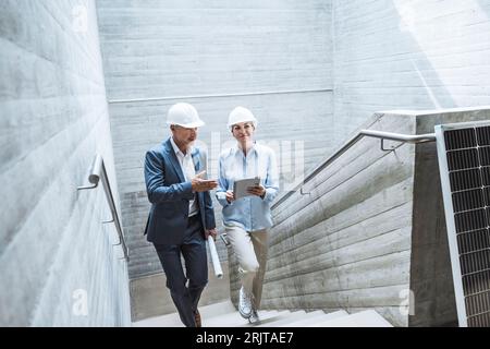 Architects discussing over tablet PC and moving up on staircase Stock Photo
