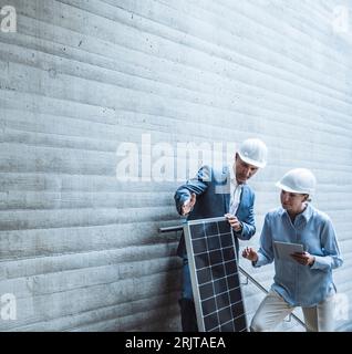 Engineers wearing hardhat and discussing over solar panel at site Stock Photo
