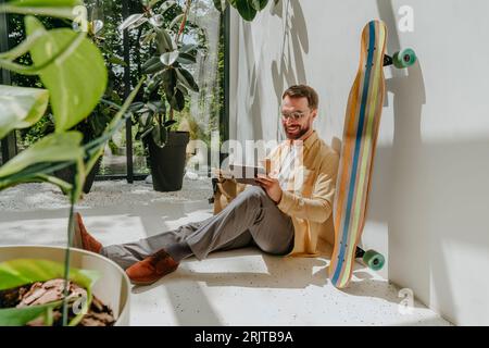 Happy businessman sitting by longboard and using tablet PC in office Stock Photo