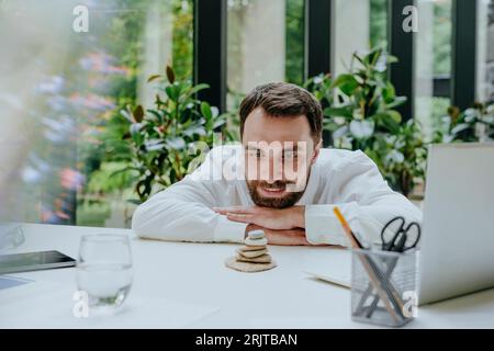 Smiling businessman looking at stack of pebble stones in office Stock Photo