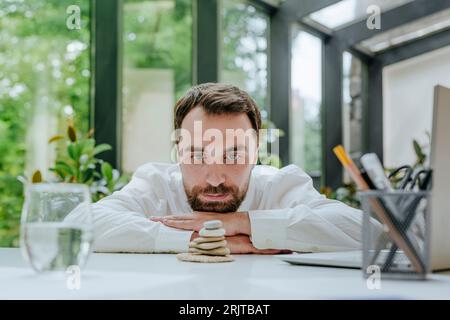 Businessman looking at stack of pebble stones in office Stock Photo