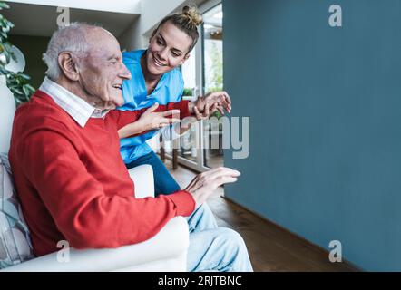 Smiling nurse helping senior man and teaching exercise at home Stock Photo