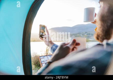 Boyfriend taking selfie with girlfriend having coffee in tent Stock Photo
