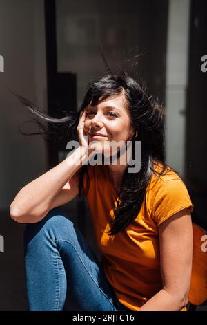 Smiling mature woman with black hair sitting on chair Stock Photo