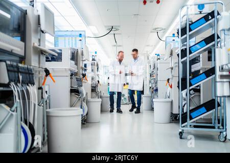 Discussing technicians walking through electronics factory holding digital tablet Stock Photo