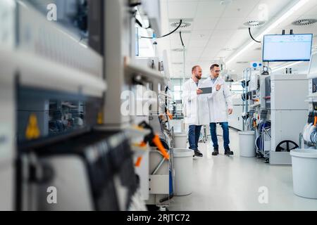 Discussing technicians walking through electronics factory holding digital tablet Stock Photo