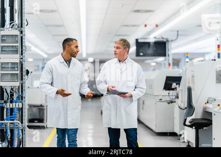 Two electrical technicians walking through factory workshop discussing over digital tablet Stock Photo