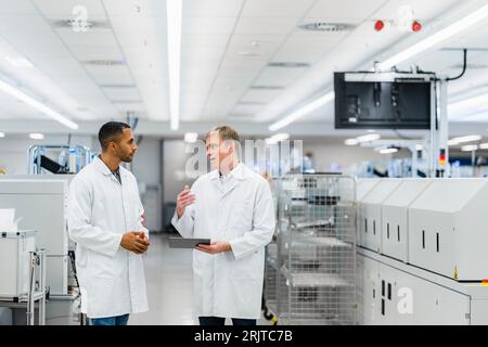Two electrical technicians walking through factory workshop discussing over digital tablet Stock Photo
