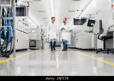 Discussing technicians walking through electronics factory holding digital tablet Stock Photo