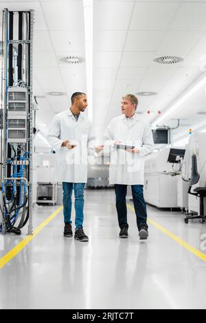Discussing technicians walking through electronics factory holding digital tablet Stock Photo