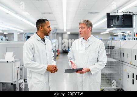 Discussing technicians walking through electronics factory holding digital tablet Stock Photo