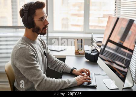 Computer programmer wearing headphones working on desktop PC in office Stock Photo