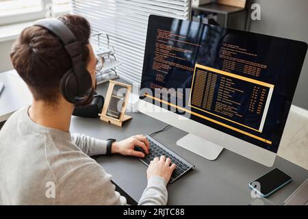 Young computer programmer wearing wireless headphones coding on computer Stock Photo