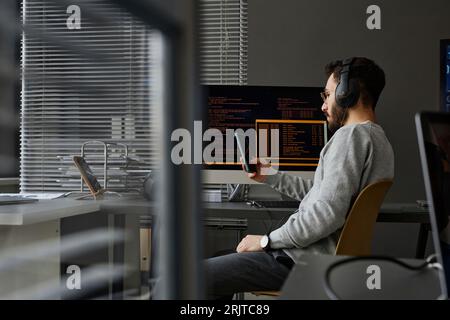 Computer programmer using smart phone at desk Stock Photo