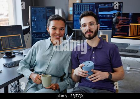 Smiling IT professionals sitting together with coffee cups in office Stock Photo