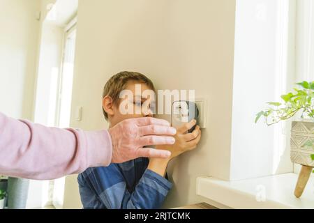 Grandfather assisting grandson to install timer in electrical outlet on wall Stock Photo