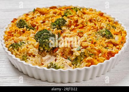 chicken rice broccoli casserole topped with cheddar cheese and crumbled cracker in baking dish on white wooden table Stock Photo