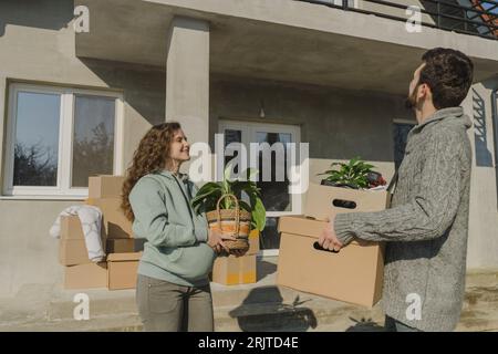 Smiling couple moving into new house carrying cardboard boxes Stock Photo
