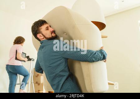 Man carrying armchair by girlfriend relocating in new house Stock Photo