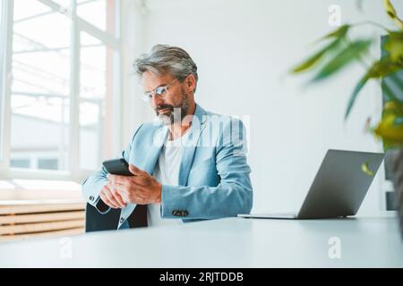Businessman using smart phone sitting at office Stock Photo