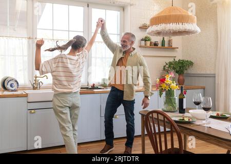 Happy mature couple dancing in kitchen at home Stock Photo