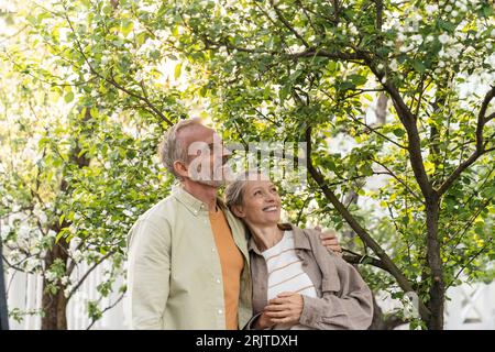 Happy couple looking up standing under tree Stock Photo