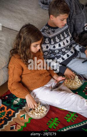 Siblings using smart phones and eating popcorn at home Stock Photo