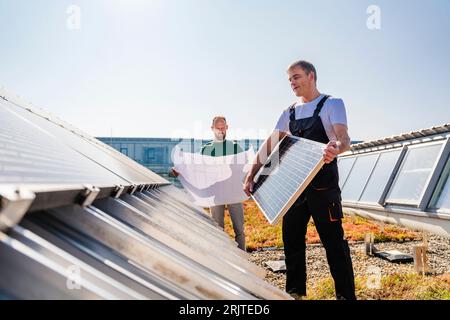 Craftsman and colleague with plan and solar panel on the roof of a company building Stock Photo