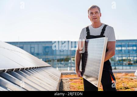 Craftsman holding solar panel on the roof of a company building Stock Photo