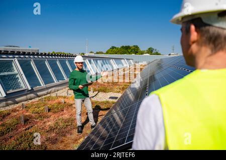 Man with tablet PC talking to colleague on the roof of a company building with solar panels Stock Photo