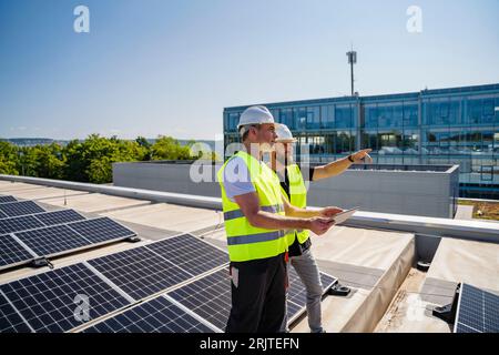Two technicians using tablet PC on the roof of a company building with solar panels Stock Photo