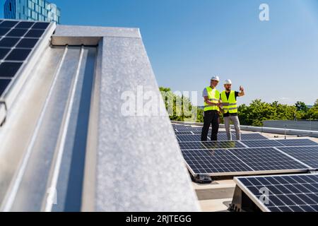 Two technicians using tablet PC on the roof of a company building with solar panels Stock Photo