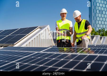 Two technicians using tablet PC on the roof of a company building with solar panels Stock Photo