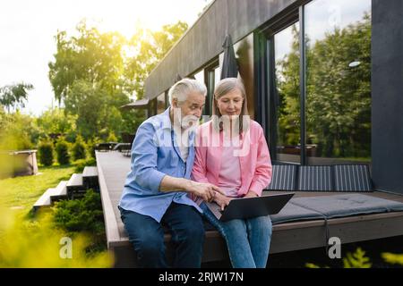 Man and woman sitting on house porch with solar panel using notebook. Stock Photo