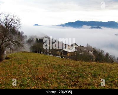 View of Gabrovo village near Skofja Loka in Gorenjska region of Slovenia surrounded by fog or mist with hills in the back Stock Photo