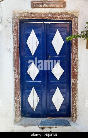 Beautiful wooden blue door, decorated with large diamond shaped white parts. Above the door, the sign says "The Boat Builder's House". Stock Photo